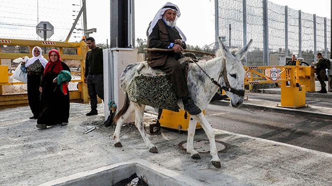 فلسطيني مسن يركب حمارًا وآخرون يعبرون نقطة تفتيش في جدار الفصل الإسرائيلي